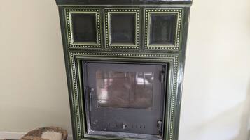 Estufa de madera estilo vintage verde con puerta de cristal, sobre un piso de baldosas, junto a una cesta tejida.