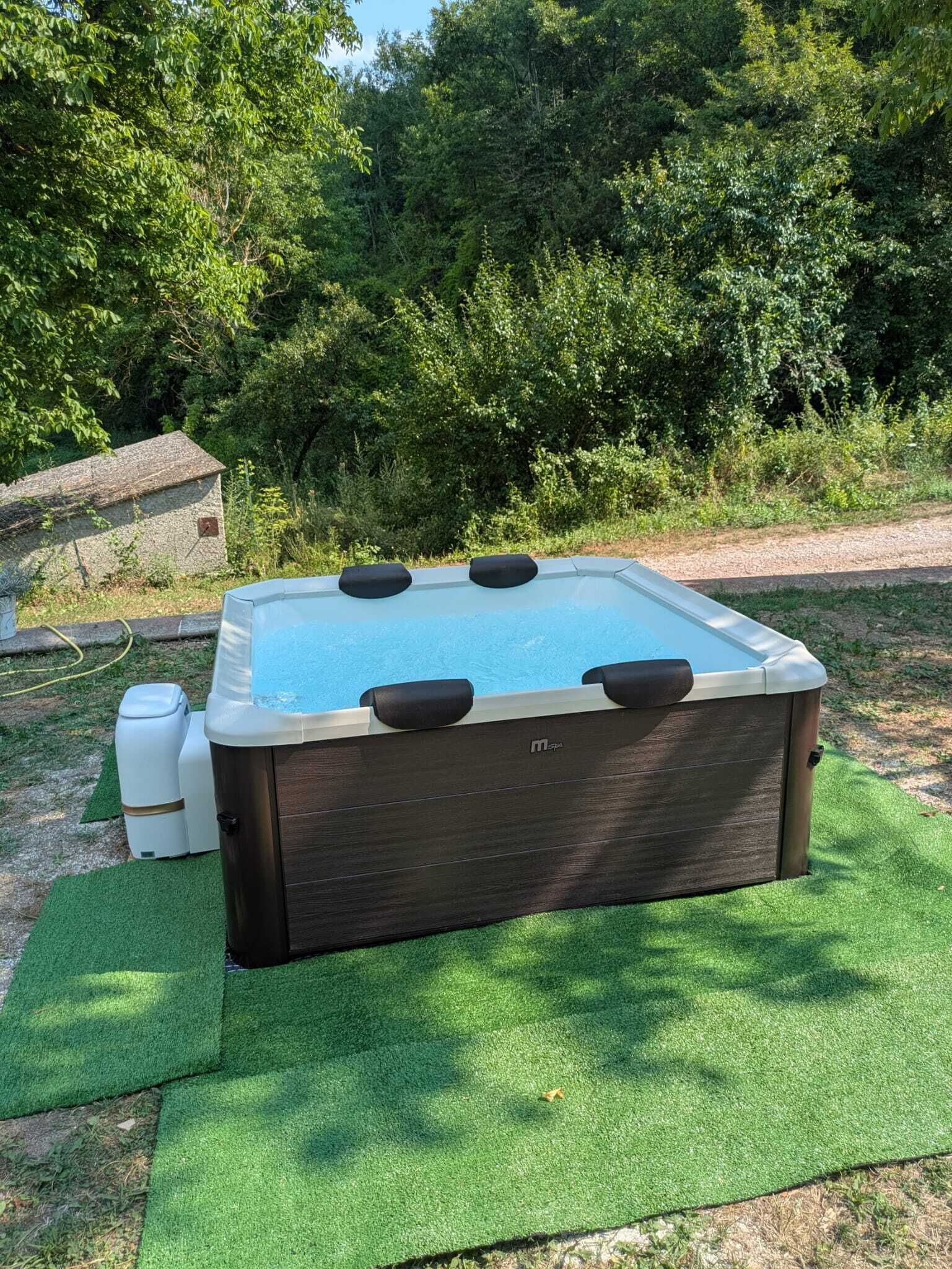 Ein rechteckiges Whirlpool mit dunkler Außenseite und heller Innenseite, umgeben von künstlichem grünen Rasen.