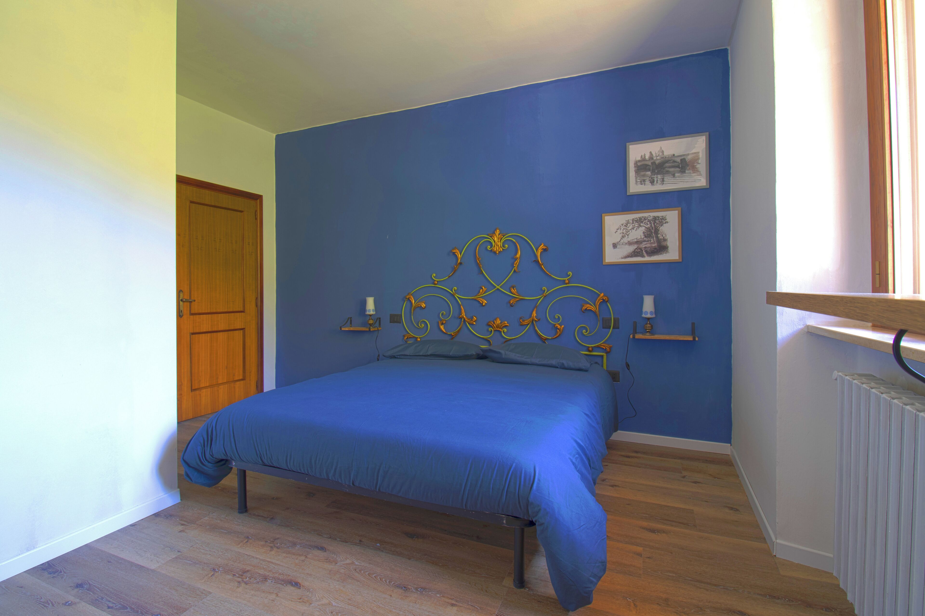 Quarto com cama, porta de madeira, parede azul e radiador.