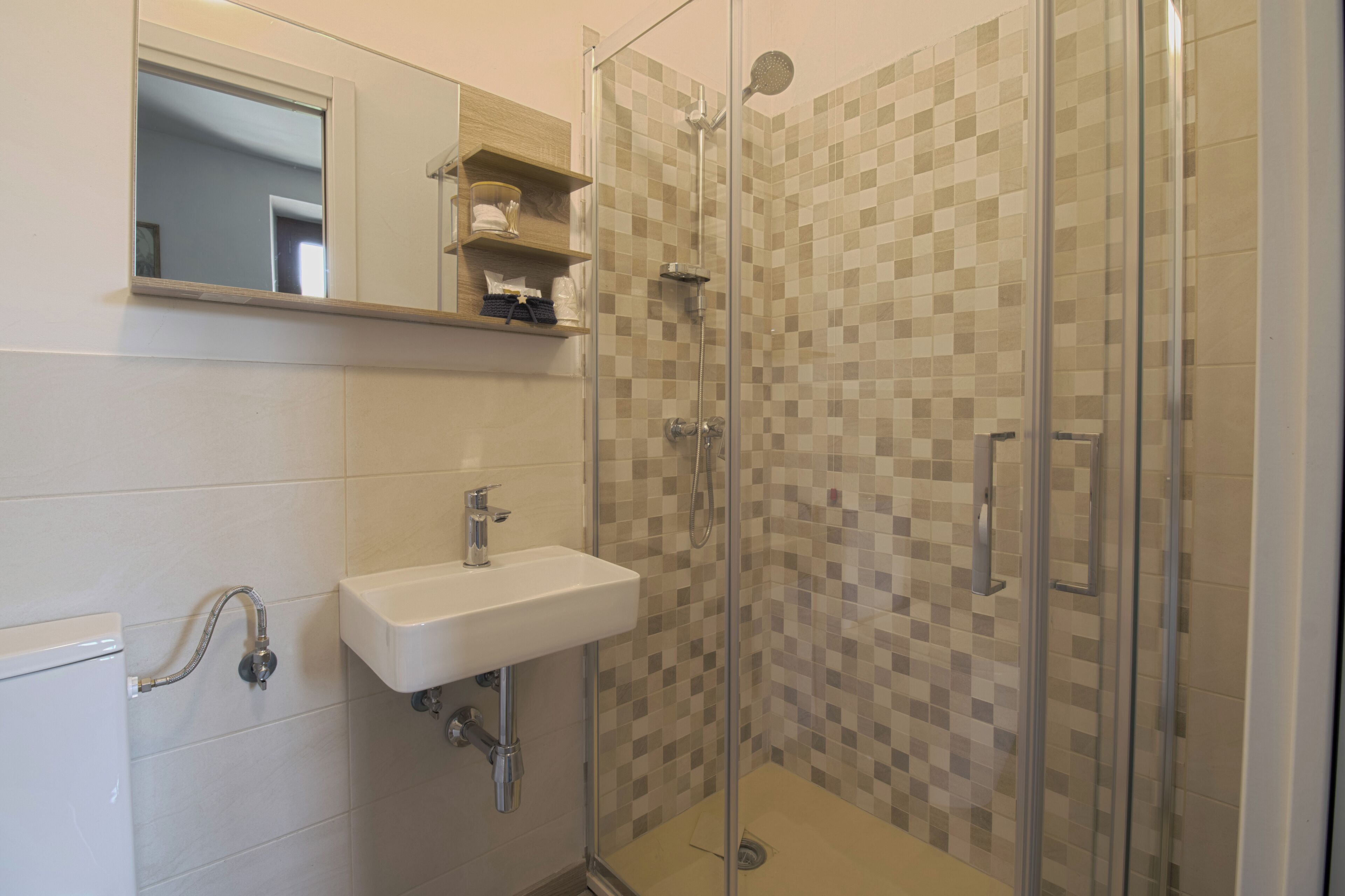 Une salle de bain avec une douche à parois de verre, un lavabo blanc et un mur recouvert de carreaux.