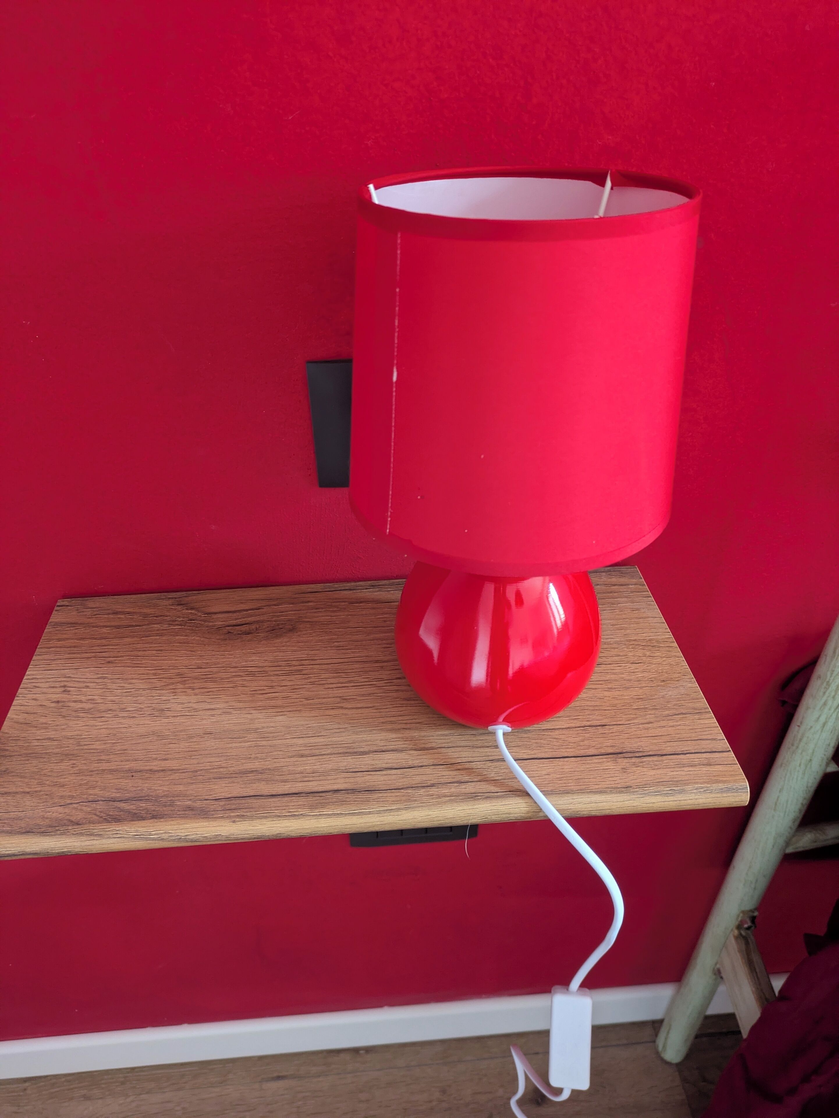 Una lámpara roja sobre un estante de madera frente a una pared roja.