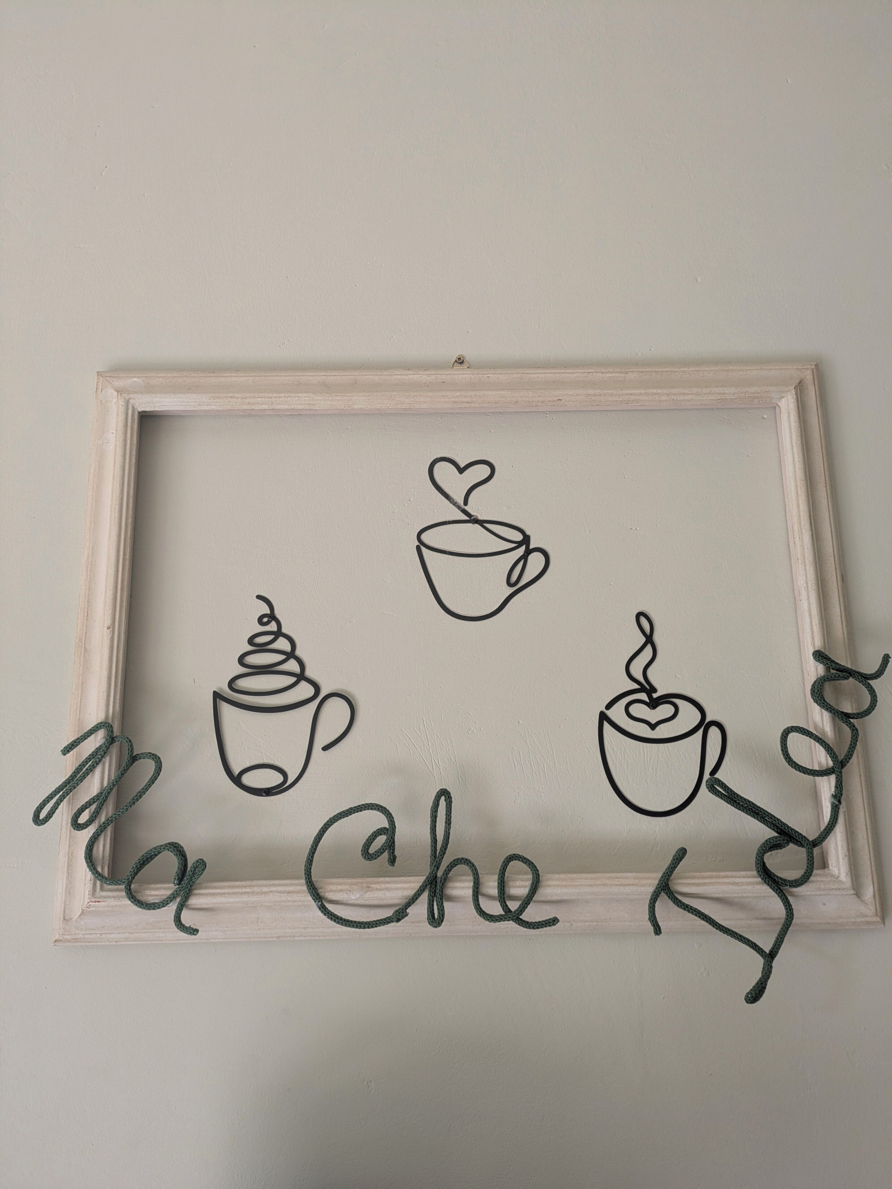 Decoración de pared en marco con diseños de tazas de café y el texto 'Ma che Kaffe'.