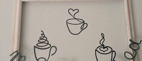 Decoración de pared en marco con diseños de tazas de café y el texto 'Ma che Kaffe'.