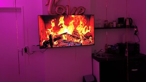 A television displaying a fire, a neon sign with the number 60, and a shelf with various items.