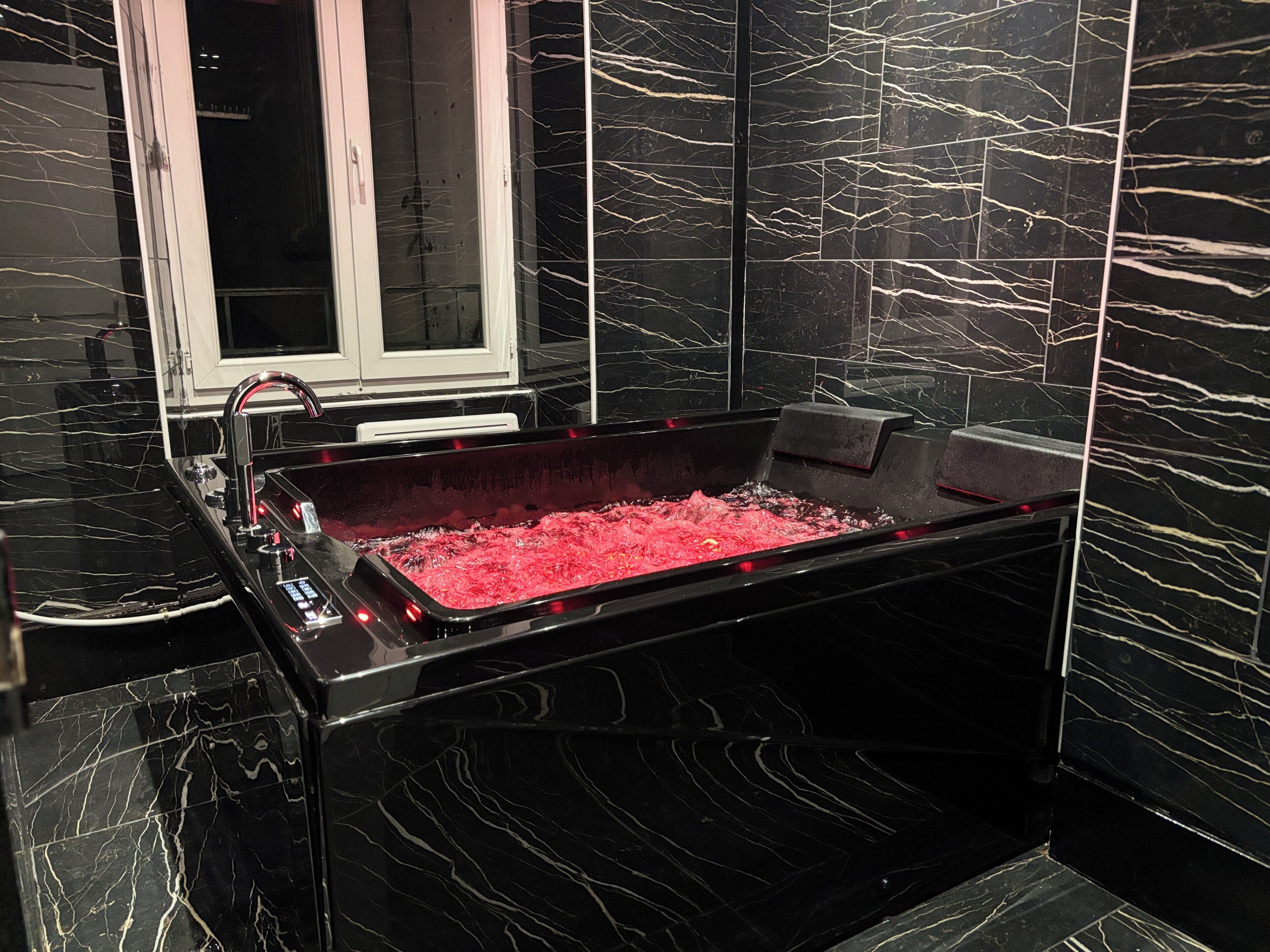 A black marble bathtub with a red interior, a window, and a modern design.