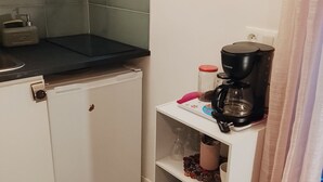 Una cocina compacta con mostrador, cafetera y una repisa con platos y un mueble pequeño.