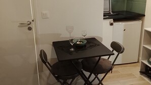 Un pequeño comedor con una mesa, dos sillas, una copa de vino y un tazón.
