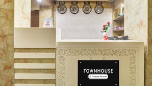 A reception desk with a 'TOWNHOUSE' sign, a clock with city names, and a vase with red flowers. - Deluxe Kunwar Aalcajars (Patna)