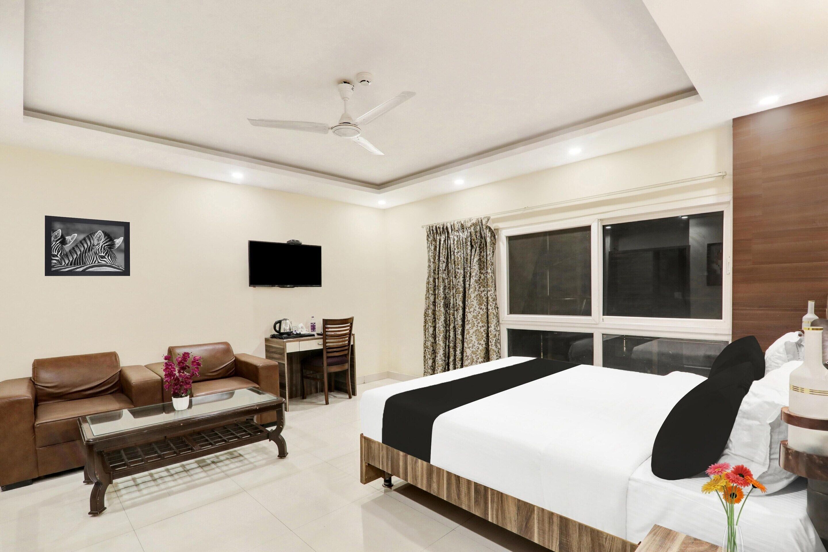 A hotel room with a bed, a sofa, a desk, a television, and a ceiling fan.