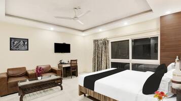 A hotel room with a bed, a sofa, a desk, a television, and a ceiling fan.