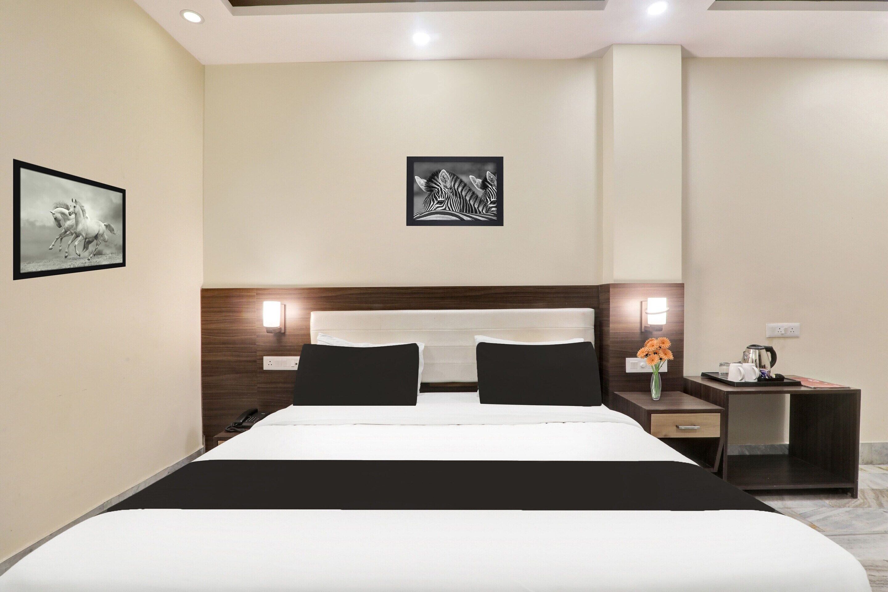 A hotel room with a bed, bedside tables, a nightstand, a vase with flowers, and wall art.