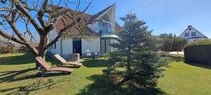 Ein Haus mit schrägem Dach, ein kleiner Garten mit Gras, ein Baum und zwei Liegestühle.