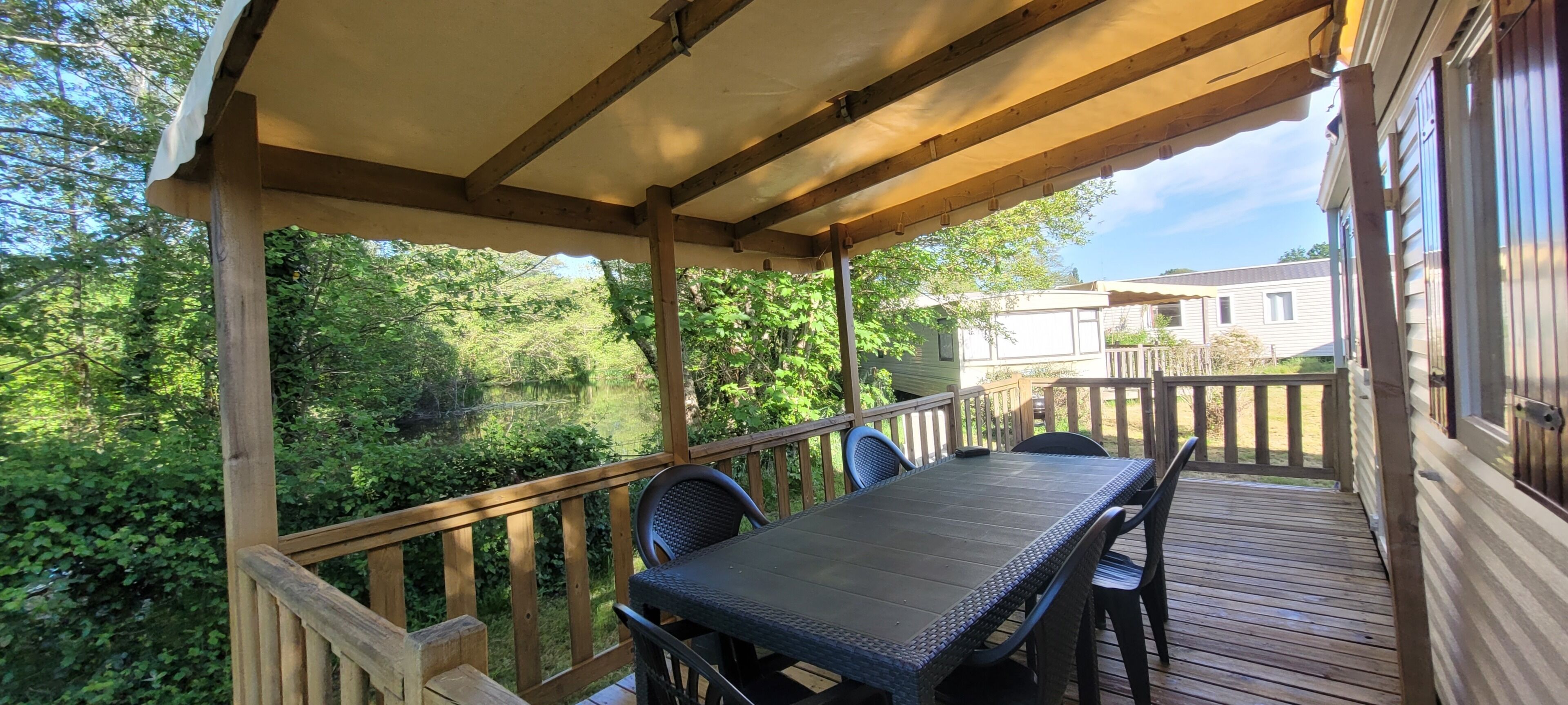 Una terraza cubierta al aire libre con una mesa y sillas, rodeada de exuberante vegetación y vistas a una casa.