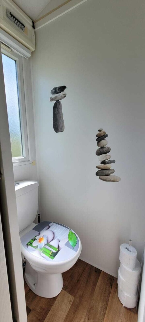 A bathroom with a toilet, a window, and a wall with a rock art installation. - Mobil-home 3★ Vendée Avrillé - 6 pers - 3 bedrooms - Pets OK (Avrillé)