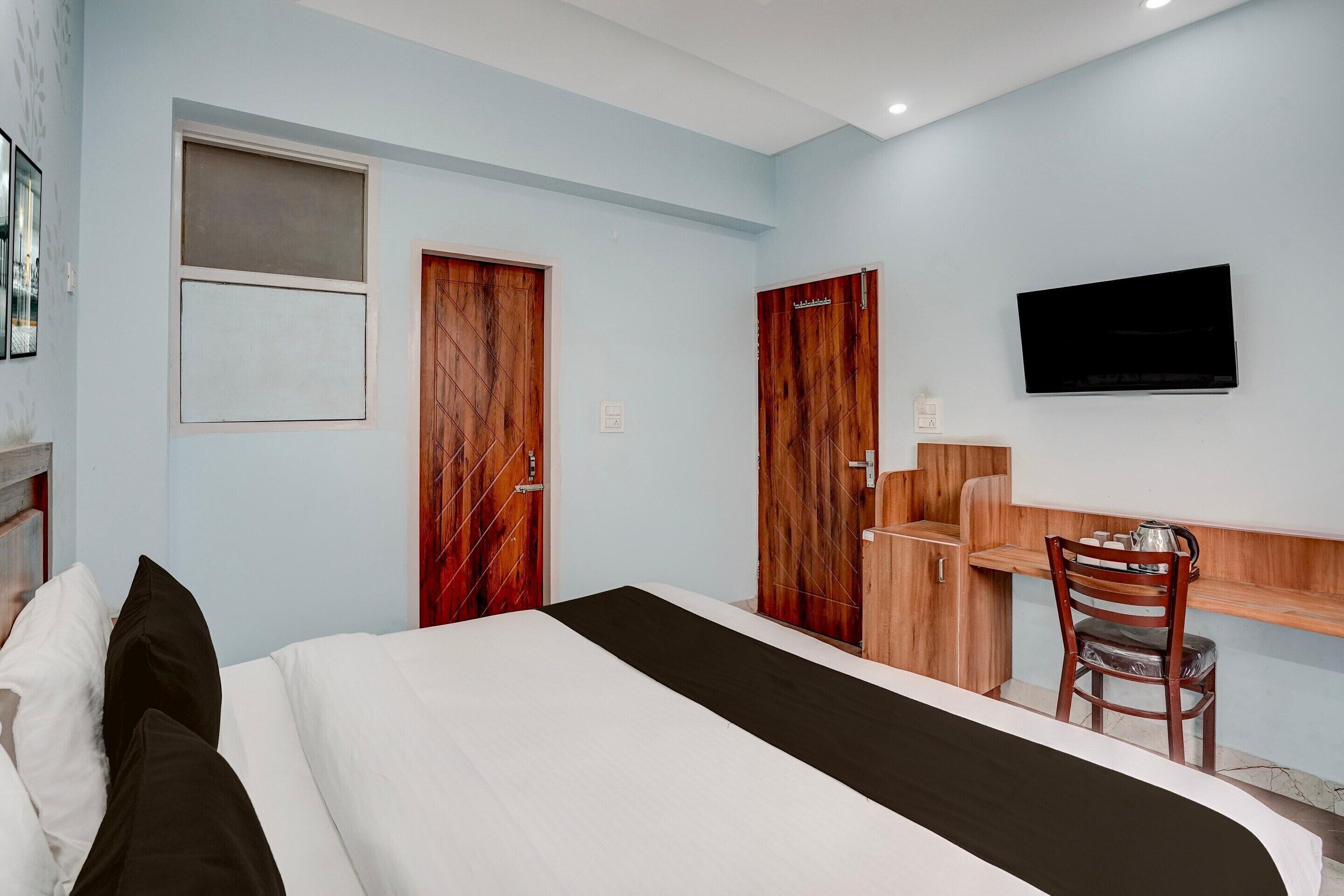 A hotel room with a bed, a desk, a chair, a television, and two wooden doors.