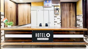 Ein Hotelrezeptionstresen mit einem Schild, das Dienstleistungen für Firmenkunden anzeigt. Holzüren und ein gerahmtes Bild hängen an der Wand.