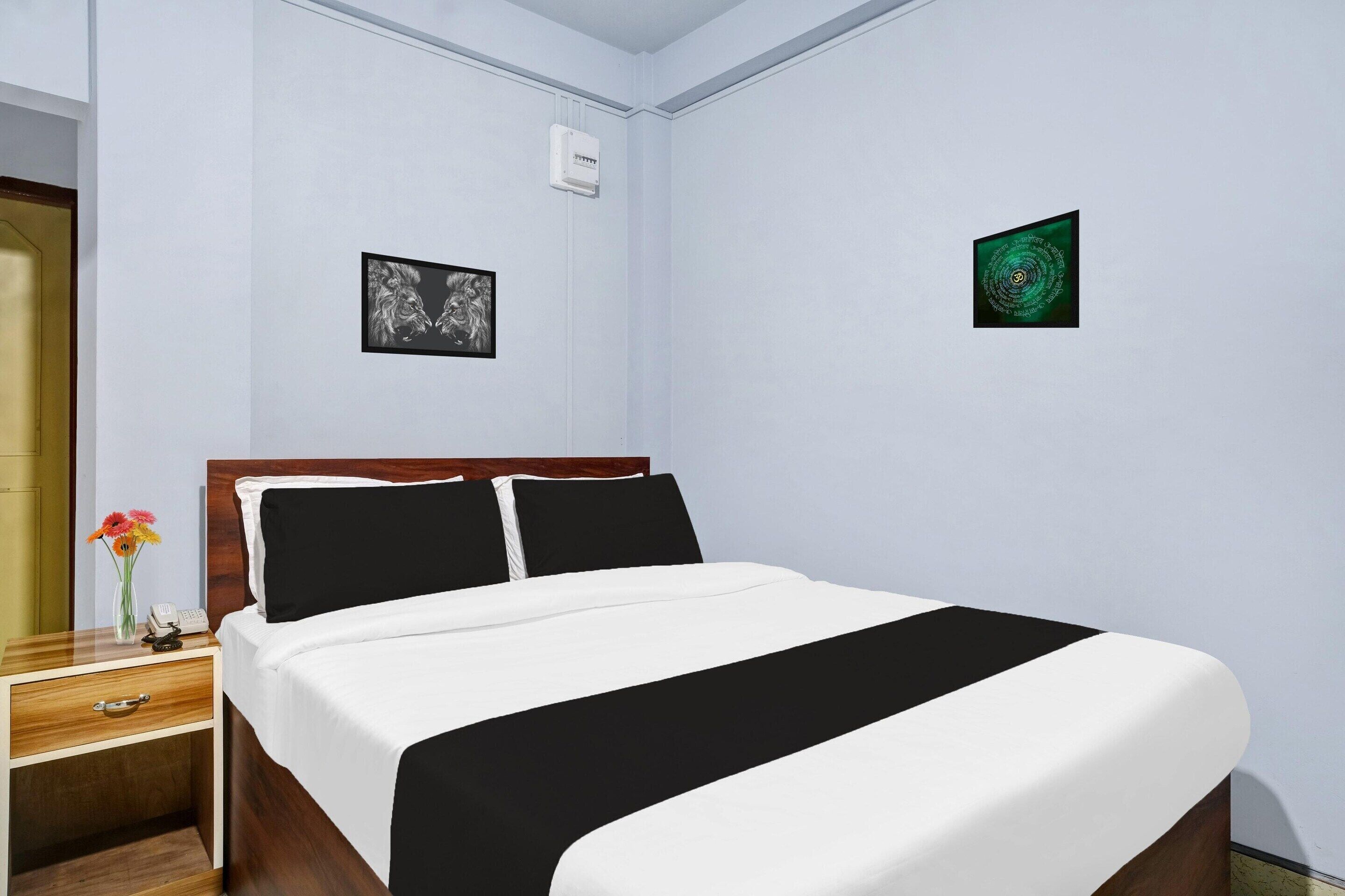 A hotel room with a bed, a nightstand with a phone and flowers, and two framed pictures on the walls.