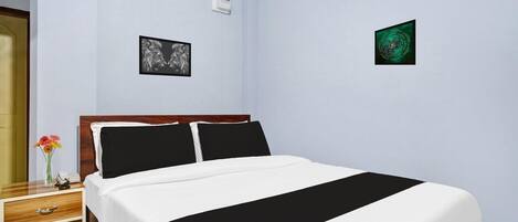 A hotel room with a bed, a nightstand with a phone and flowers, and two framed pictures on the walls.