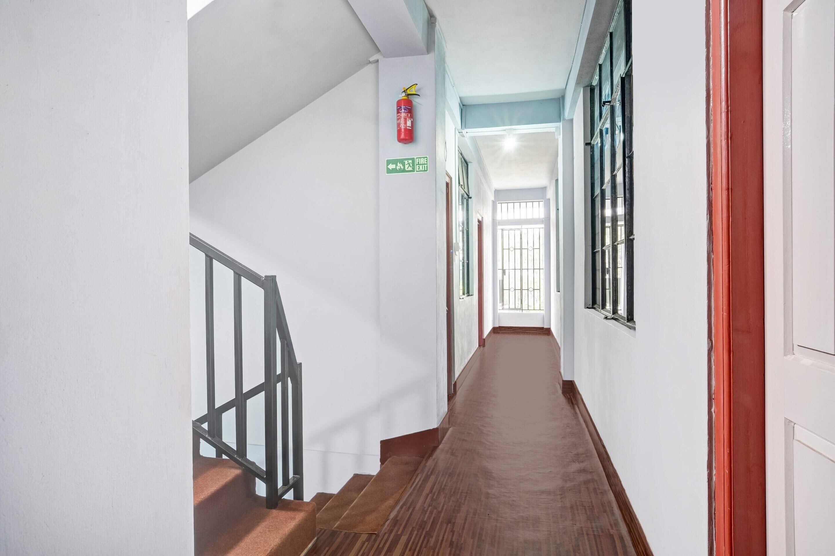 A hallway with a wooden staircase, a fire exit sign, and a window with bars.