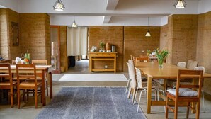 Una habitación amplia con una gran mesa de comedor de madera, sillas de mimbre y una alfombra gris.