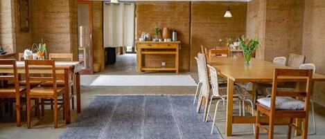 A spacious room with a large wooden dining table, wicker chairs, and a grey rug.
