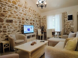 Ein Zimmer mit Steinwänden, einem Fernseher, Sofas, einem Couchtisch und einem Essbereich.