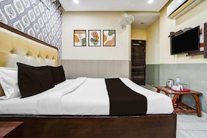 A hotel room with a bed, a TV mounted on the wall, and a small table with a kettle and a water bottle.