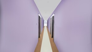 A hallway with purple walls and a white floor, leading to a door at the end.