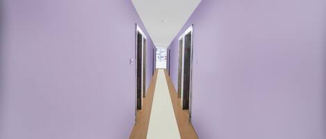 A hallway with purple walls and a white floor, leading to a door at the end.