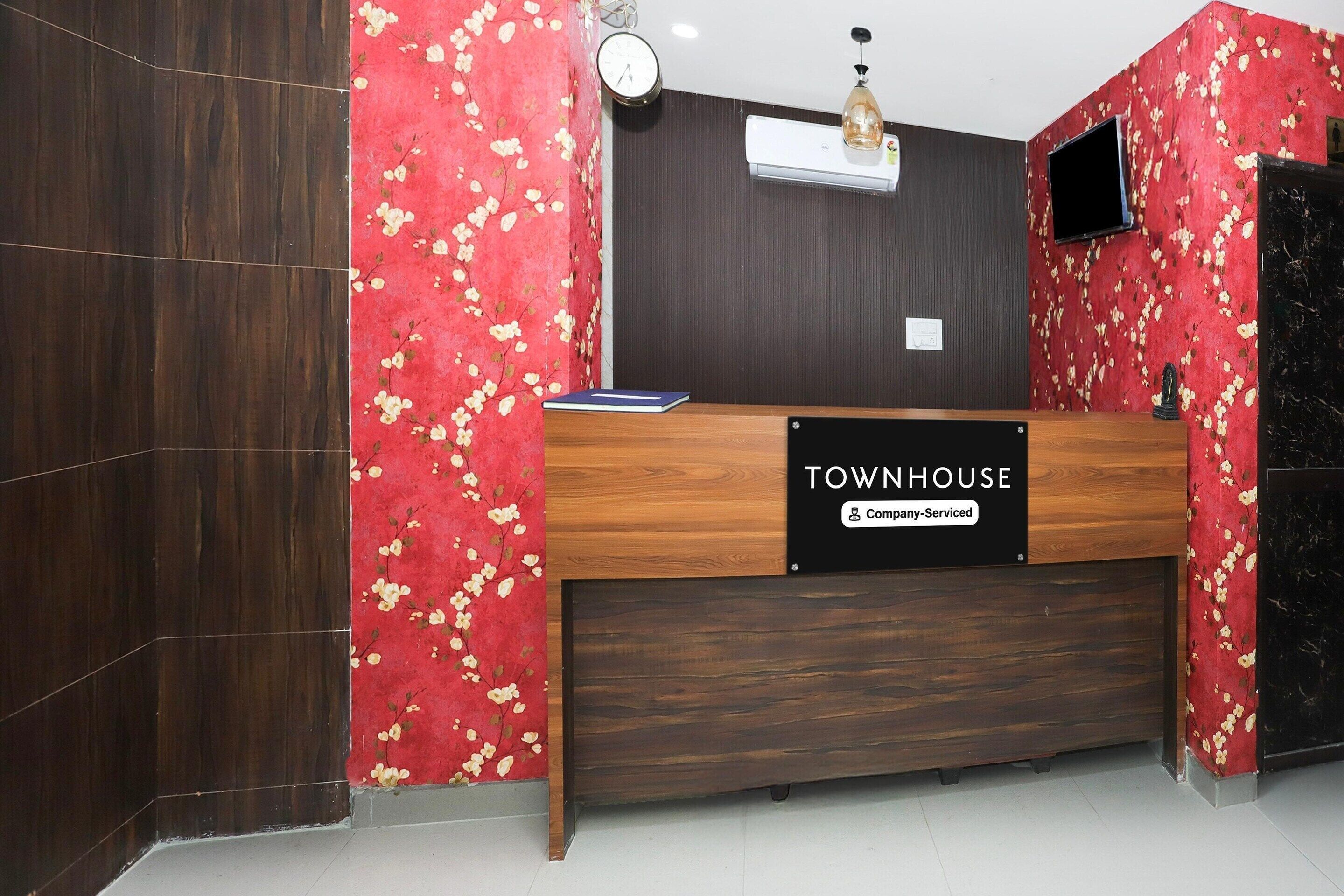 Un mostrador de recepción con un cartel que dice 'TOWNHOUSE & Company-Serviced', un reloj y un televisor montado.