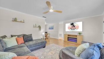 Un salon comprenant un canapé, une table basse, un ventilateur de plafond, une cheminée et un écran de télévision affichant le texte « Place To Be Renais ».