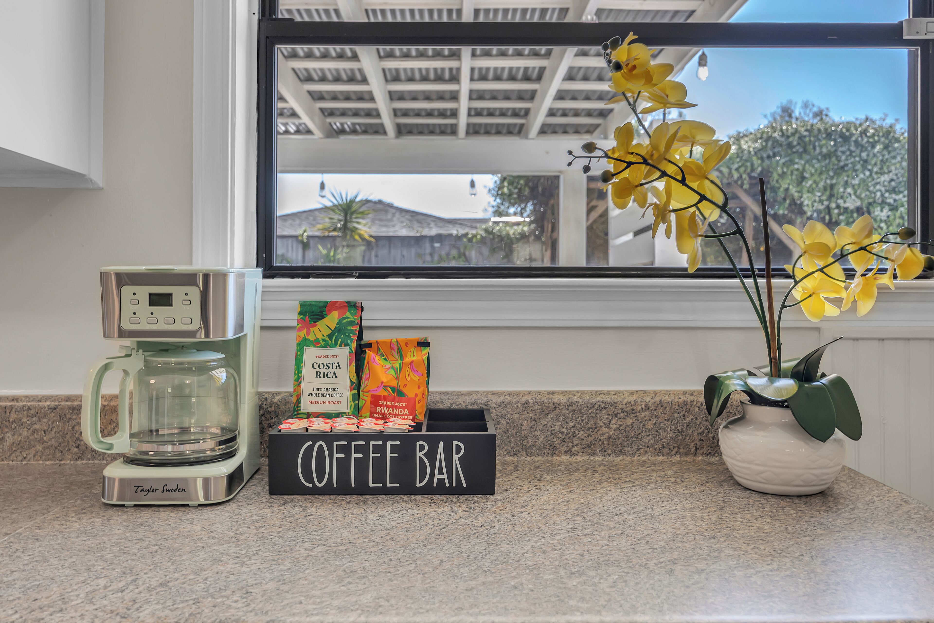 A coffee bar setup with a coffee maker, coffee bags, and a sign.