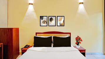 A hotel room with a bed, a nightstand with a phone, a vase with flowers, and three framed pictures on the wall.