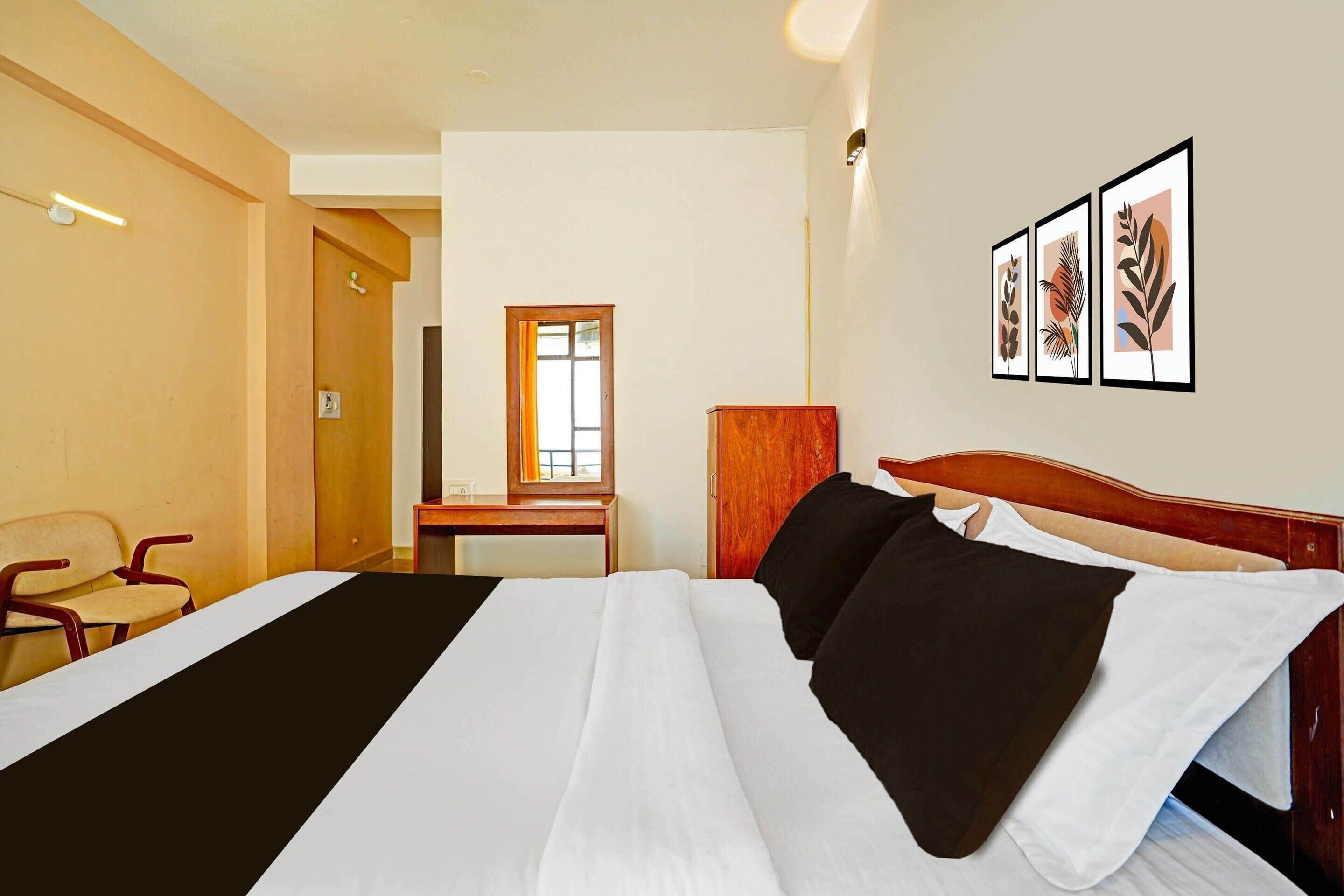 A hotel room with a bed, a desk, a chair, and framed artwork on the wall.