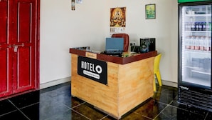 Un comptoir d’accueil portant l’inscription « HOTELO », équipé d’un ordinateur, d’une chaise et d’un réfrigérateur rempli de boissons.
