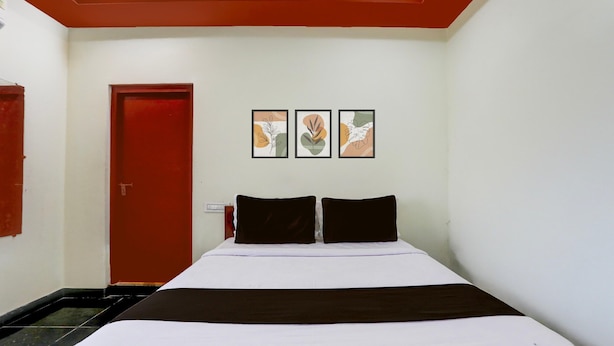 Une chambre d’hôtel avec un lit, une porte rouge et trois tableaux encadrés accrochés au mur.