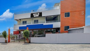 Un hôtel de deux étages au design moderne, avec une enseigne « HÔTEL  » bien visible, une entrée couverte et une allée d’accès fermée par un portail.