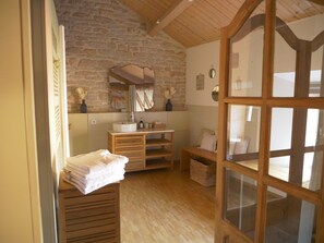 A rustic bathroom with a stone wall, wooden vanity, and a large mirror.
