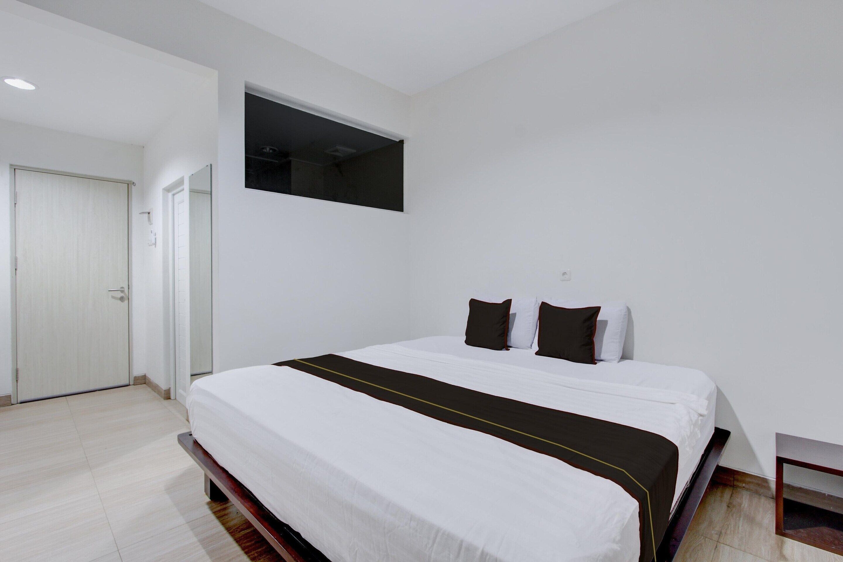 Quarto de hotel com cama, porta e uma pequena mesa.
