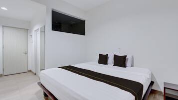Quarto de hotel com cama, porta e uma pequena mesa.