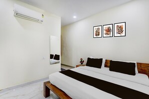 Ein Hotelzimmer mit einem Bett, einem Nachttisch mit Blumen in einer Vase, einer Wand-Klimaanlage und drei gerahmten Pflanzenbildern.