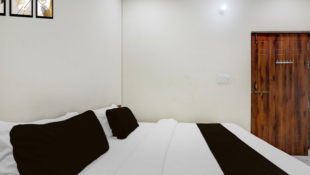 A room with a bed, a wooden door, and a wall-mounted light fixture. - Super Deluxe Room Skd Hotel and Banquet (Bakshi Ka Talab)