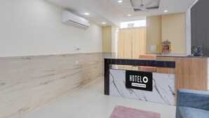 A hotel reception area with a marble reception desk, a wooden wall, a ceiling fan, and a window with curtains. - Super Deluxe Room Skd Hotel and Banquet (Bakshi Ka Talab)