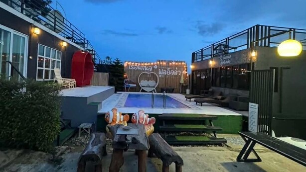 Zona de piscina exterior con un escenario, asientos y un cartel con escritura tailandesa.