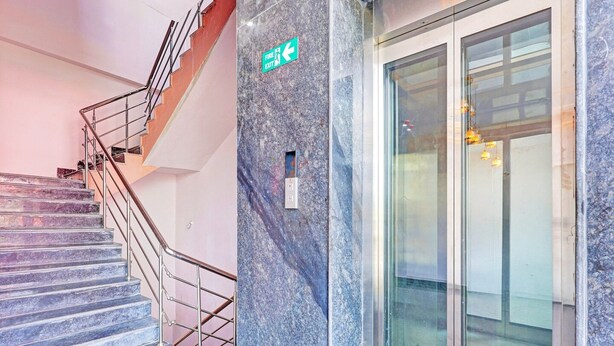 A staircase with a metal railing, a fire exit sign, and a glass door with a reflection.