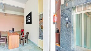 A hotel reception area with a wooden desk, chairs, a sign indicating hotel services, a fire extinguisher, and a marble wall.