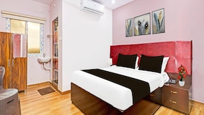A hotel room with a bed, bedside table, nightstand, and a window with blinds.