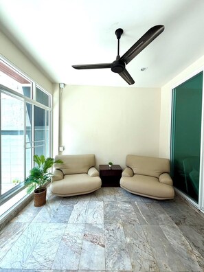 Ein modernes Wohnzimmer mit Deckenventilator, zwei beigefarbenen Sofas, einem kleinen Tisch mit Pflanze und einem großen Fenster.