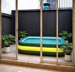 Ein kleiner, abgeschlossener Bereich mit einem aufblasbaren Pool in Grün und Gelb, Blumentöpfen und einer dunklen Wand.