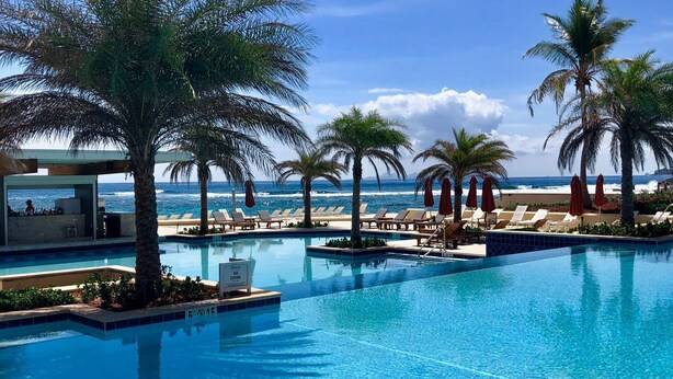 A clear blue pool with lounge chairs and palm trees, overlooking the ocean. - Saint Martin Dawn Beach Club 2027 (SINT MARTEEN)